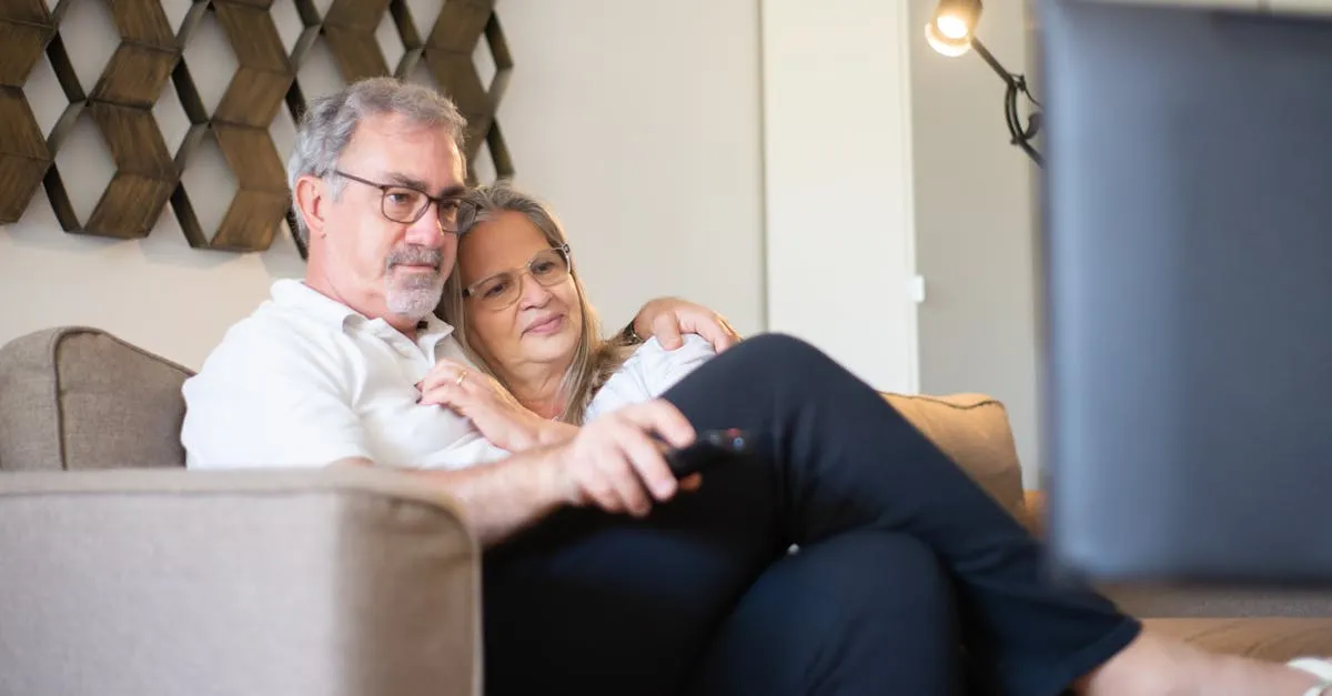 Senior couple comfortably watching TV together in their living room with wireless headphones
